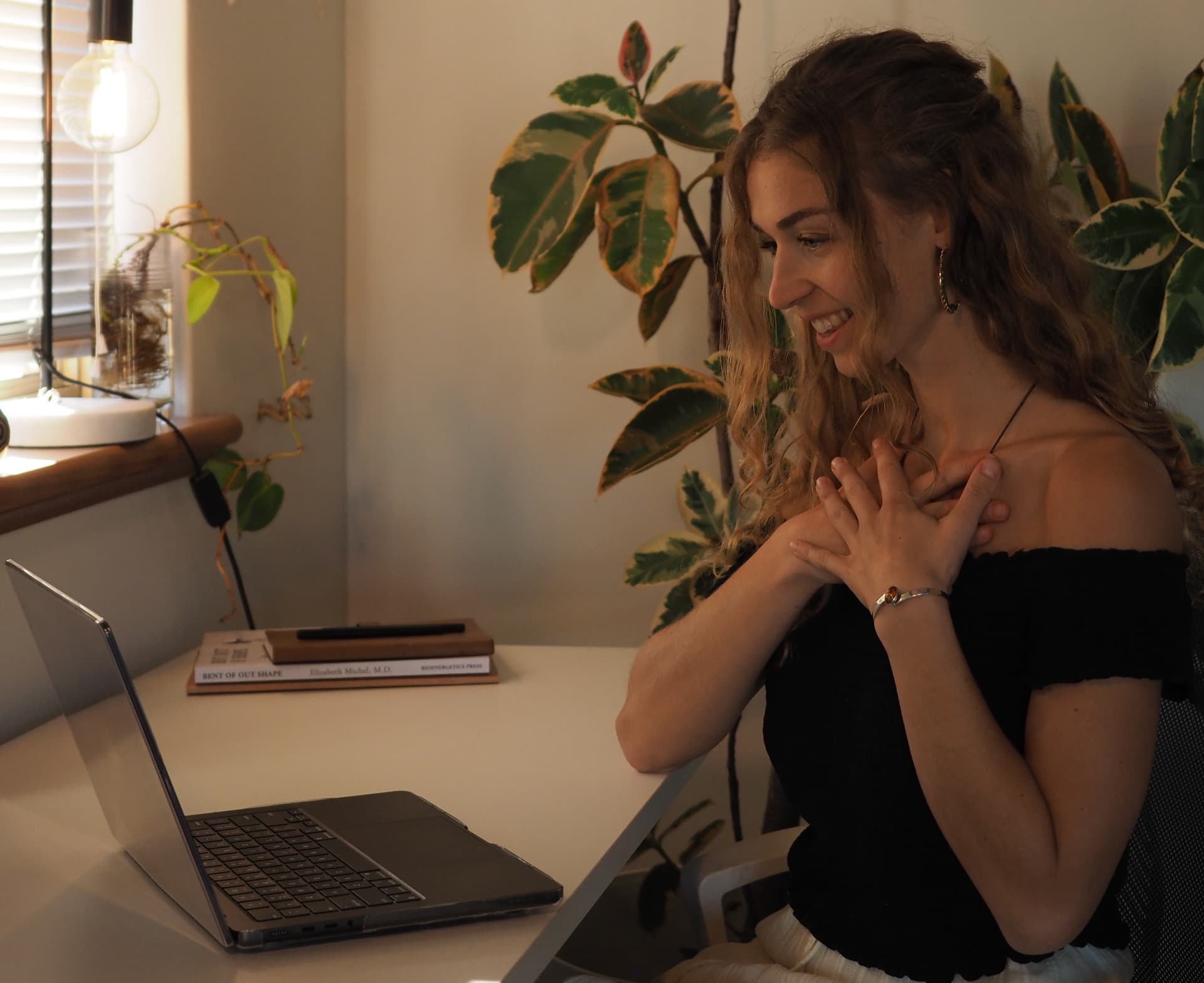 Anna-Lena smiling with her hands resting on her chest beside her laptop during an online session