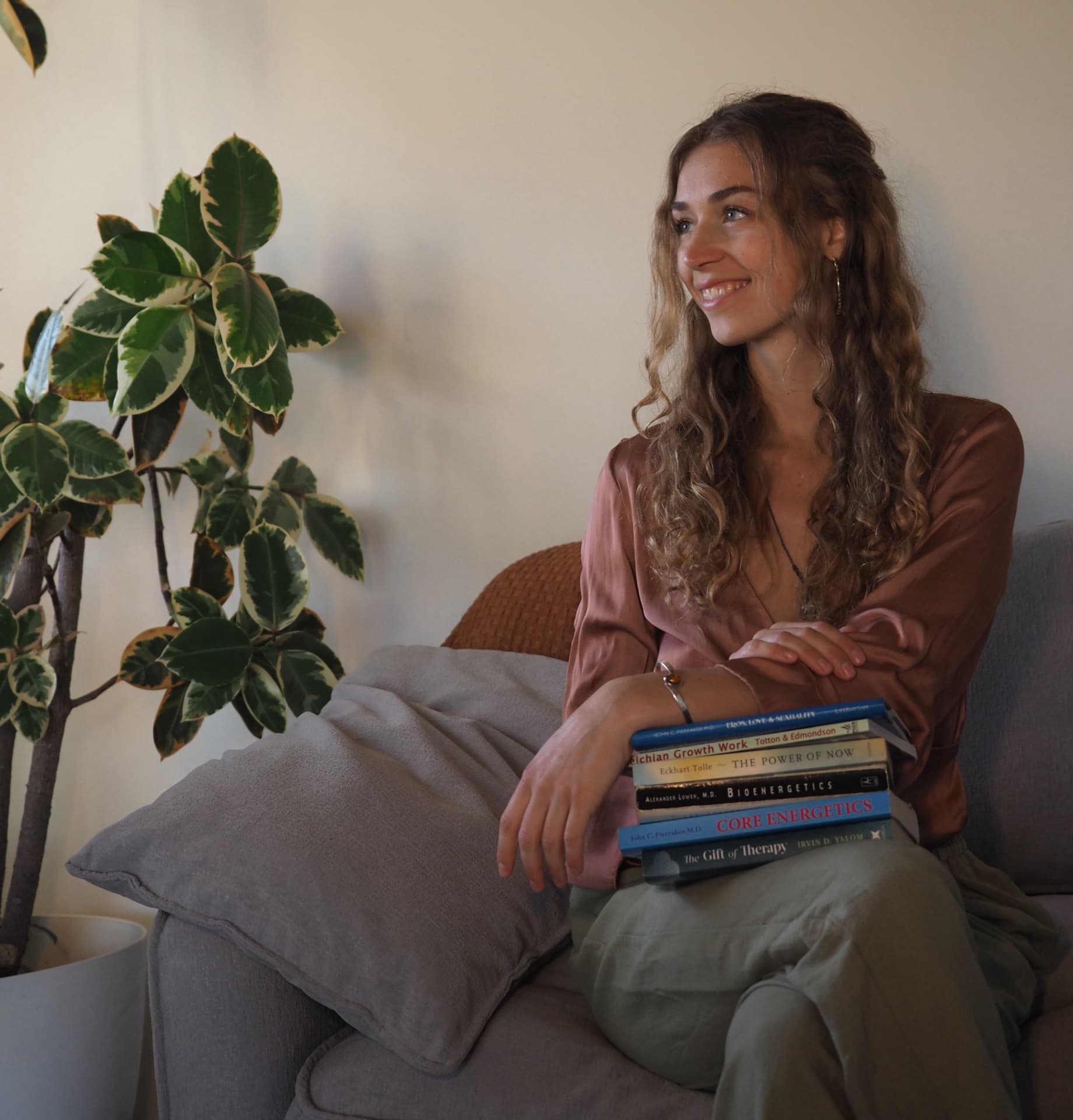 Anna-Lena seated indoors with psychotherapy books and a leafy plant